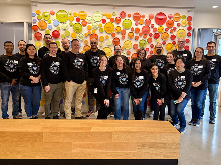 Group of employees in matching shirts standing in front of yellow, orange and red circles on a wall.