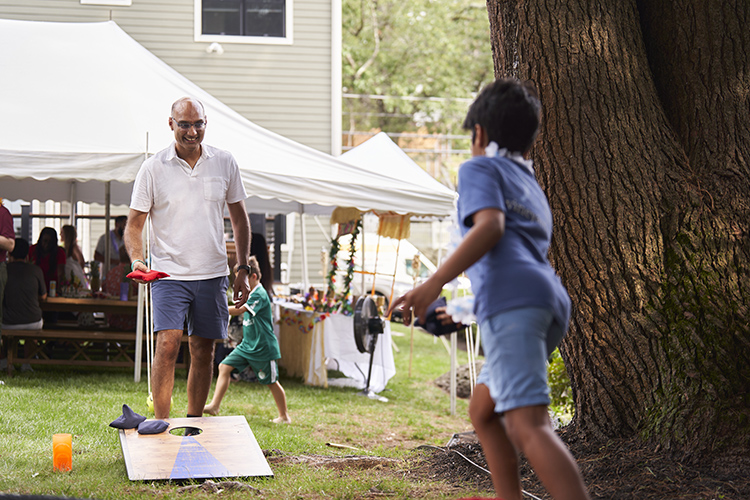 Adult man and a child playing cornhole at a summer event